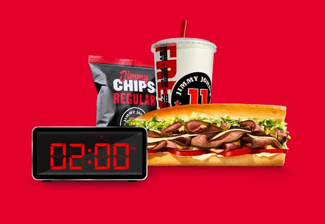 Red background, with an alarm clock displaying 2AM. Behind it is a sandwich, chips and drink.