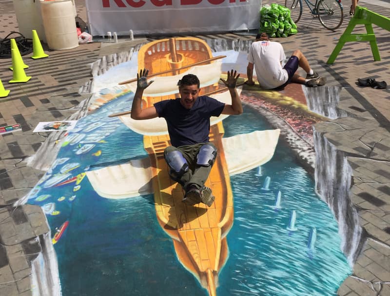 Ignacio Garcia poses with one of his chalk murals depicting a classic sail boat.